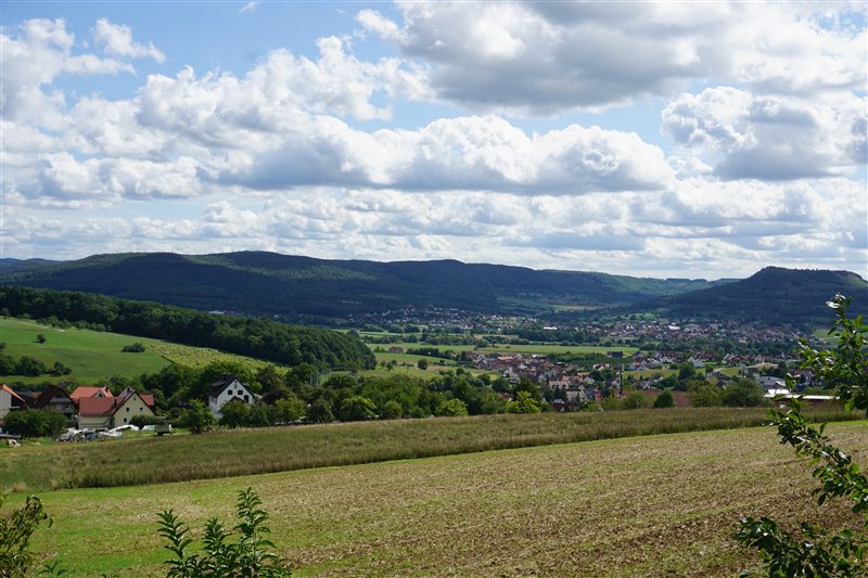Fields and a village beneath wooded hills and a sky filled with clouds